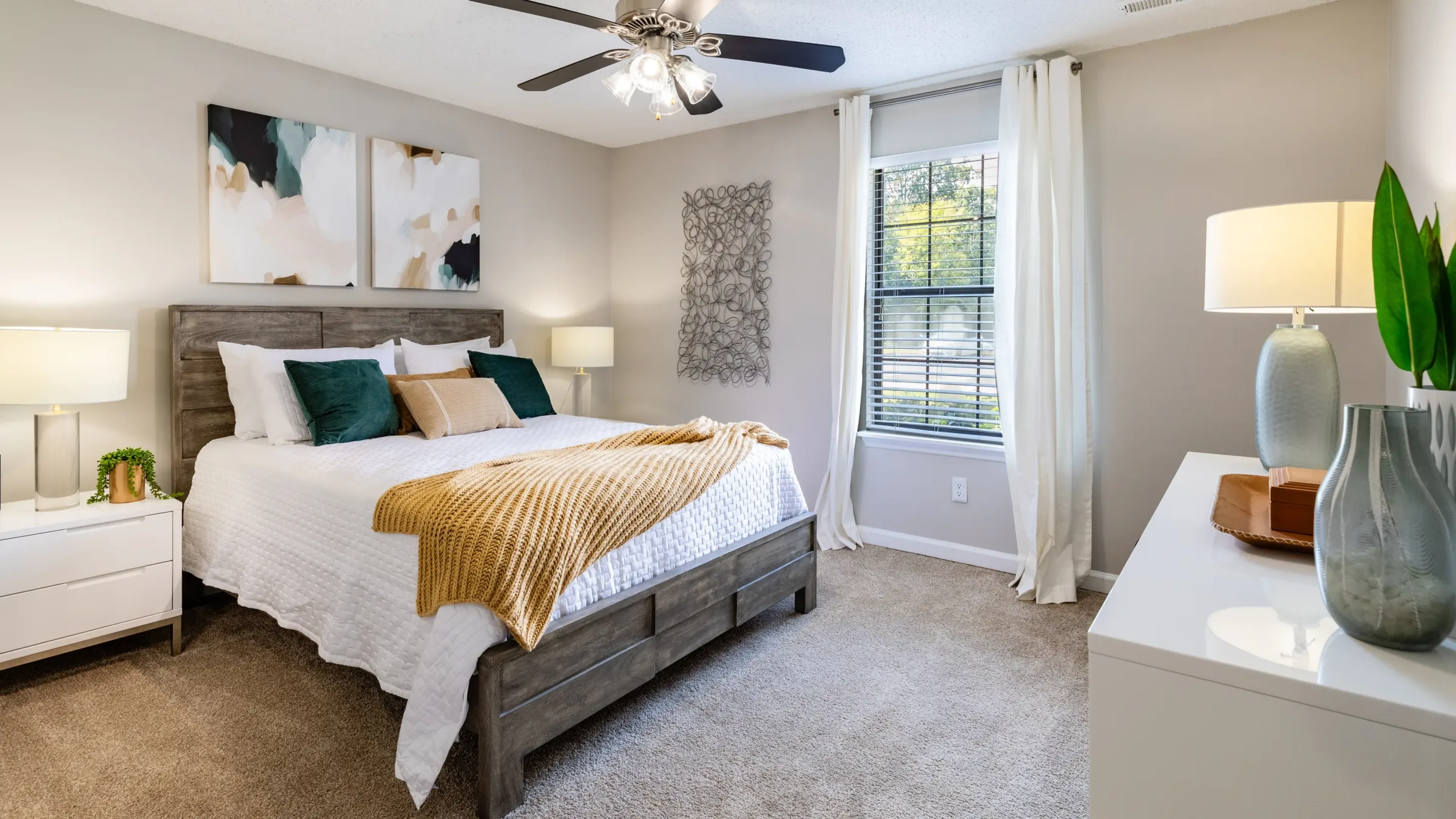 Hawthorne at the Ridge apartment bedroom with large window, ceiling fan, carpeted floors, and a bed with 2 side tables